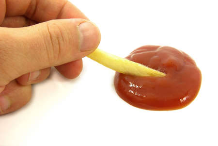 Studio shot of a hand holding a chip dipped into ketchup.