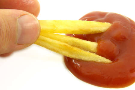 Studio shot of a hand holding French fries dipped into ketchup.