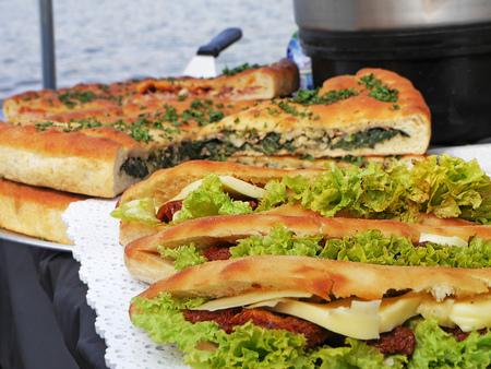 Ham and cheese salad submarine sandwich from fresh baguette. Baked vegetable pie with spinach in the background.の写真素材