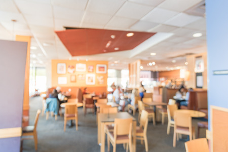 Blurred abstract background interior of counter-serve bakery, cafe chain shop in USA. Wooden table chair in compact design, natural light from windows. Customer enjoy sandwiches, salads, bread, coffeeの写真素材