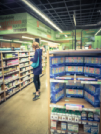 Blurred motion a skinny woman looking for supplement product from a shelf while shopping at local drugstore. Healthcare medicine buyer customer retail purchasing pickingの写真素材