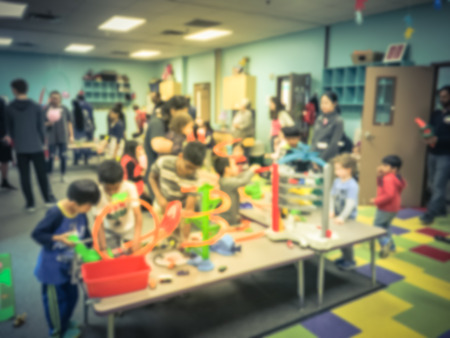 Blurred motion kids and parents enjoy playing toys car track racing indoor. Abstract background diverse, multicultural group of people gathering together near Dallas, Texas, USAの写真素材