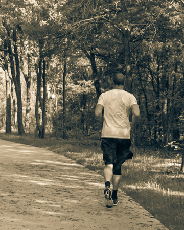 Vintage tone rear view of senior Caucasian man running at nature park during sunset. Healthy person in white crew shirt and long sock running on concrete pathway in natural area in Texas, USAの写真素材
