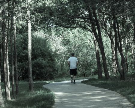 Senior Caucasian man running at nature park during sunset. Rear view of healthy person in white crew shirt and long sock running on s-curved concrete pathway in natural area near Dallas, Texas, USAの写真素材