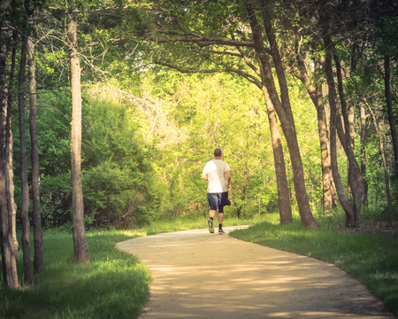 Senior Caucasian man running at nature park during sunset. Rear view of healthy person in white crew shirt and long sock running on s-curved concrete pathway in natural area near Dallas, Texas, USAの写真素材