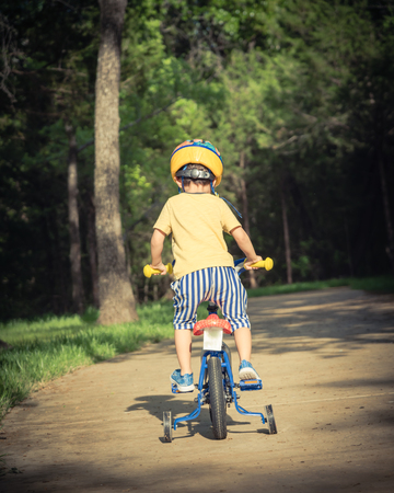 Filtered image back view of healthy Asian kid riding bicycle in the American parkの写真素材