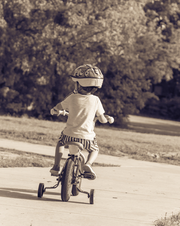 Filtered image back view of healthy Asian kid riding bicycle in the American parkの写真素材