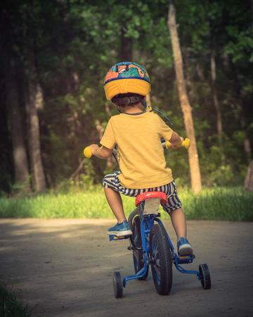 Filtered image back view of healthy Asian kid riding bicycle in the American parkの写真素材