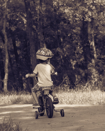 Filtered image back view of healthy Asian kid riding bicycle in the American parkの写真素材