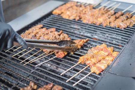 Asian lady hand with glove turns skewer on grilling racksの写真素材