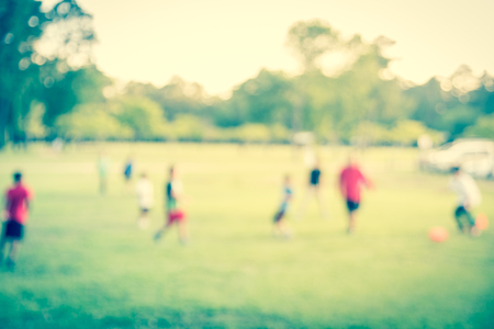 Filtered image blurry background coach playing soccer with boys at park during sunsetの写真素材