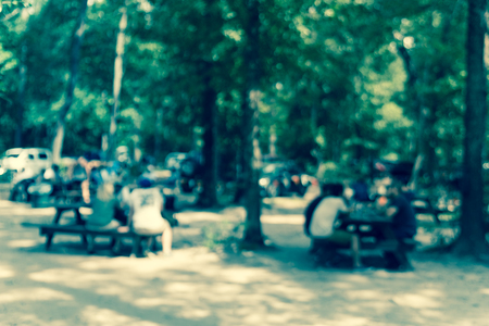 Vintage tone blur image group of people hanging out at semi forest, wooded area of craft brewery in Conroe, Texas, US. Beer garden fill with picnic tables, long benches setup under tall oak treesの写真素材
