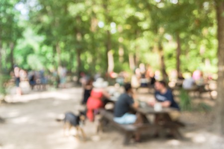 Blur image group of people with leashed dog hanging out at semi forest, wooded area of craft brewery in Conroe, Texas, US. Beer garden fill with picnic tables, long benches setup under tall oak trees.の写真素材