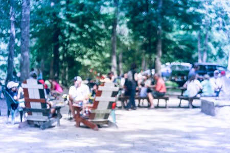 Blur image group of people hanging out at semi forest, wooded area of craft brewery in Conroe, Texas, US. Beer garden fill with picnic tables, long benches setup under tall oak trees. Park activities.の写真素材