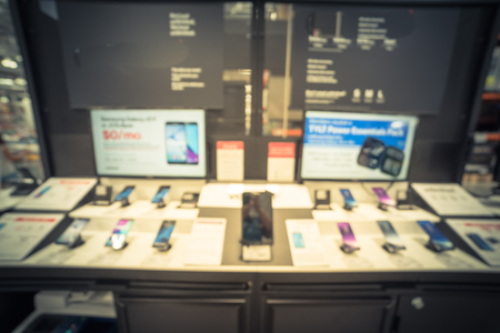 Blurred variety of modern smart phones on display at cell phone department in distribution warehouse or storehouse. Defocused background of technology inventory, hypermarket, wholesale bokeh light.の写真素材
