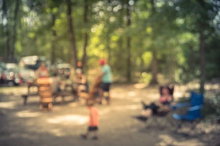 Blur image group of people hanging out at semi forest, wooded area of craft brewery in Conroe, Texas, US. Beer garden fill with picnic tables, long benches setup under tall oak trees. Park activities.の写真素材