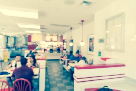 Vintage tone blurred image a compact fast food restaurant in Austin, Texas, USA. People serving sauce, ketchup and enjoying lunch with burgers, fried fries and sugar drinkの写真素材
