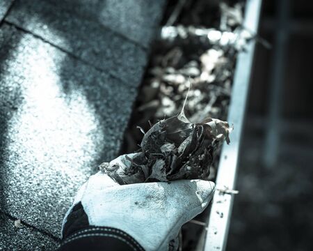 Top view man hand in gloves cleaning house gutter from leaves and dirt. Roof gutter cleaning near...