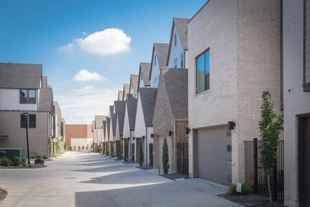 Large back alley of new development residential community with metal fence gate and well trim landscape outside of downtown Dallas, Texas. Row of two car garages from modern three story housesの写真素材
