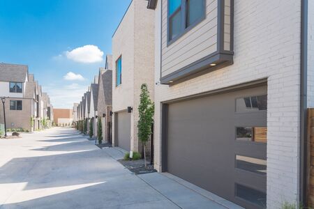 Row of garages from modern three story houses in North Dallas, Texas. Large back alley of new development residential community with metal fence gate and well trim landscapeの写真素材