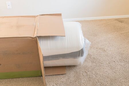 Top view brand new roll-packed spring mattresses on carpet floor of apartment bedroom in Texas, America. Foam and latex hybrid material mattress being unboxed from cardboard boxの写真素材