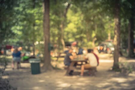 Blur image group of people hanging out at semi forest, wooded area of craft brewery in Conroe, Texas, US. Beer garden fill with picnic tables, long benches setup under tall oak trees. Park activities.の写真素材