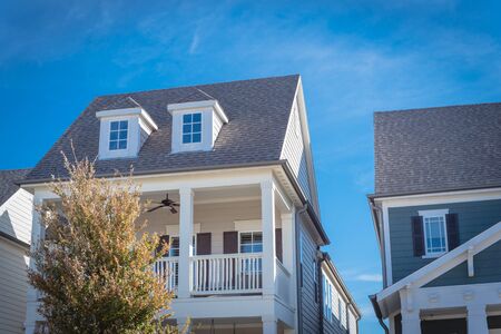 Second story porch with white painted outer edge and banister. Dormer roof windows with weathered shingle siding tiles under cloud blue sky. Country âstyle houses in suburbs Dallas, Texas, USAの写真素材