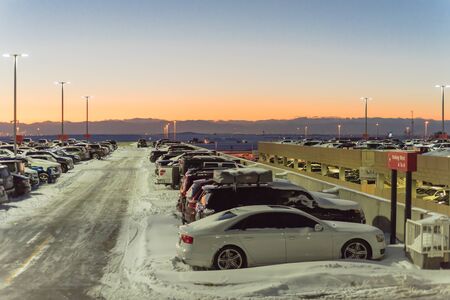 Full terminal parking at Denver International Airport (DIA) in frosty cold autumn sunset. Row of cars at busy parking lot with snowdrifts during severe weather condition in Colorado, USA.の写真素材