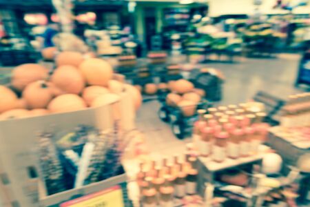 Vintage tone blurred image Halloween decoration inside grocery store in Houston, Texas, USA. Pile of pumpkins on hay, corns, garden cart wagon and scarecrow on display. Holiday festive backgroundの写真素材