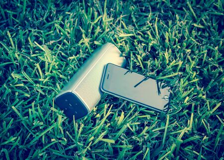 Smart phone and wireless speaker on grass lawn outdoor at sunset.の写真素材