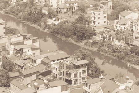 Top view polluted To Lich River and dense of multi story residential houses along the bank. Aerial view urban sprawling concrete home with red metal roof in suburbs Hanoi, Vietnam.の写真素材