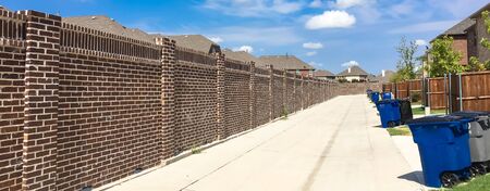 Panorama view clean back alley of new development neighborhood in Allen, Texas, US in cloud blue sky. Two story house with wooden fence and brick wall screen and row of trash and recycle binsの写真素材
