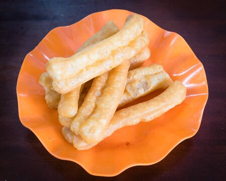 Top close-up Youtiao or cakwe or Chinese cruller, fried breadstick, fritters, oil stick, doughnut, char in orange plate on wooden table. Often served with noodle and soup in Vietnamese cuisines.の写真素材
