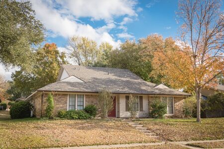 Typical front yard of single family houses near Dallas, Texas in fall season with colorful autumn leaves. Elevated sidewalk of one story house under mature trees with cloud blue skyの写真素材