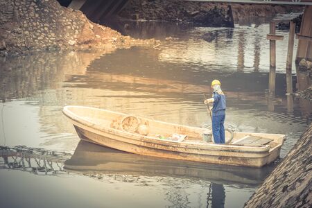 Polluted river in Hanoi with high embankment, retaining wall and a female worker is cleaning variety of wastes on the canal. Pollution is one of the most serious problems of Vietnamの写真素材