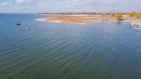 Large lake with safety marker buoy and anglers fishing from motor boats near rolling shoreline at...