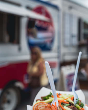 Motion blurred food truck and customer background with selective focus on paper food tray of chicken...