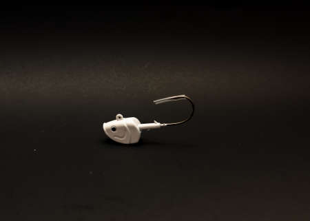 One white shad jig head with plastic fishing hook tip cover isolated on black background. Metal bass...