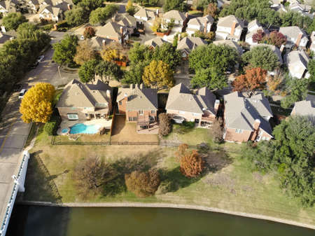 Top view waterfront two story houses with metal fence near canal bridge and colorful fall foliages in suburbs Dallas, Texas, USA. Aerial view residential neighborhood autumn leaves backgroundの写真素材