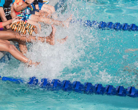 Group of diverse multiethnic children kicking splashing water at poolside of swimming class in North Texas, America. Kids with swimwear at swimming pool class learning to swimの写真素材