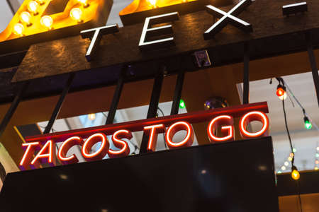 Colorful light bulb and red LED Tacos to go text at Tex Mex restaurant in Texas, America. Lookup view of large Taco take away text at modern airport restaurant.の写真素材