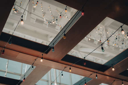 Toned photo colorful light bulb string on ceiling near glass roof and wooden exposure beam structure of terminal airport bar in Houston, Texas, USA. Modern design interior, furniture backgroundの写真素材