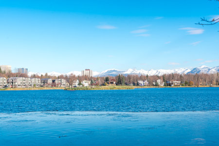 Westchester Lagoon with small island on the lake and row of duplex houses with downtown Anchorage...