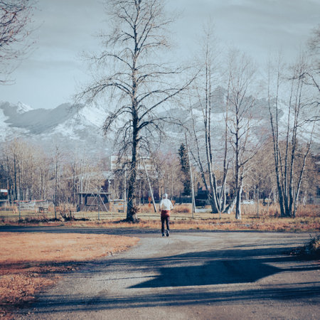 Toned photo rear view Caucasian man in warm clothes running along gravel trail near Lake Spenard, snow cap Chugach Mountain in background, Anchorage Alaska. Healthy active outdoor lifestyleの写真素材