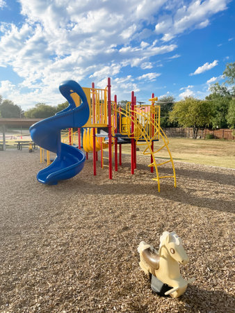 Typical horse spring riders and colorful playground under sunny blue cloud sky at elementary school...