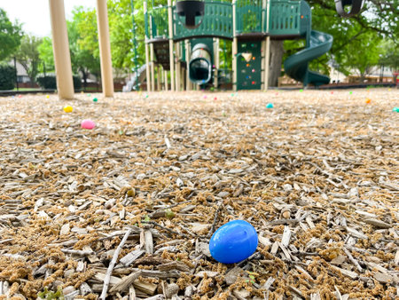 Close-up plastic egg with candy inside and blurry playground background for kids Easter egg hunt activity near Dallas, Texas, America. Seasonal children and family holiday traditional activitiesの写真素材