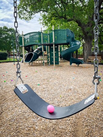 Colorful plastic egg with candy inside on swing with blurry playground background for kids Easter egg hunt activity Dallas, Texas, USA. Seasonal children and family holiday traditional activitiesの写真素材