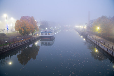 Historic Erie Canal in Fairport village with barge cruise boat tour, foggy morning mist and reflection of colorful fall foliage along riverside walk, Upstate New York, USA. Scenic small-town Americaの写真素材