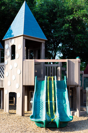 Wooden playground with canopy and plastic triple slide under construction yellow caution tape...