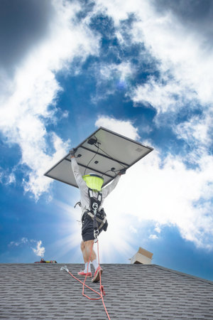 Worker with fall protection rope lifeline, safety harness carrying solar panel walking on shingle...